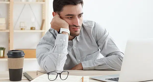 a man is in sitting front of his laptop tired and unable to focus 