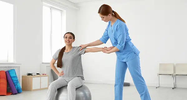 a female provider in blue scrubs helps a patient dressed in grey with her shoulder pain