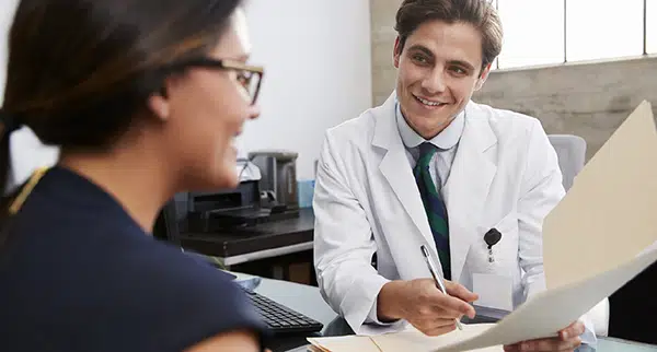 a doctor and a patient sit at a desk discussing follow-ups