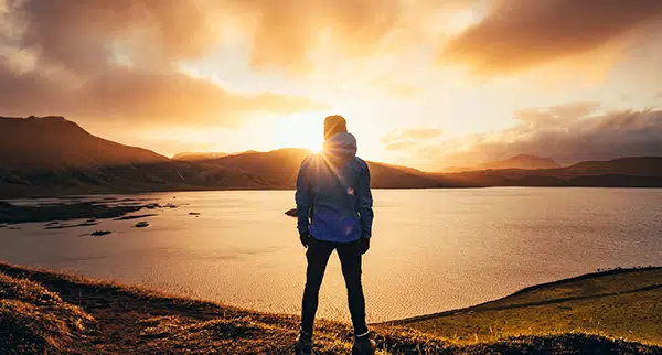 a man stands admiring the sunrise at the edge of a lake after recovering from chronic pain