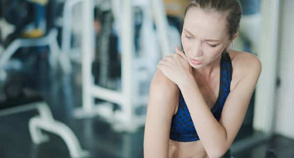 a woman massages her shoulder after a workout has caused her pain